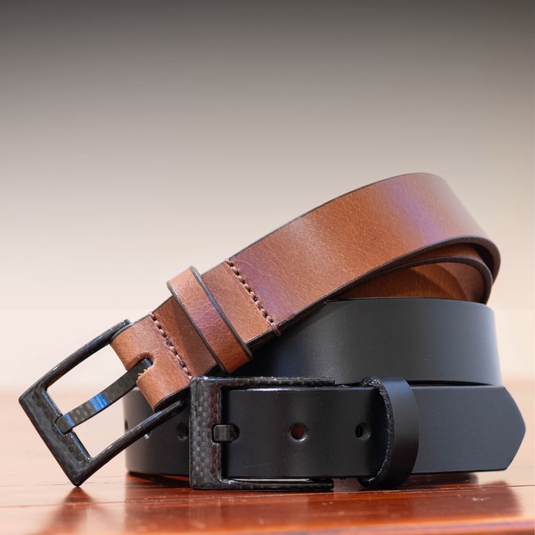 Brown and black leather belts on a wooden surface with a gradient background
