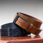 Two leather belts, one brown and one black, on a wooden surface with a neutral background.