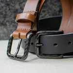 Image of Black and brown leather belts with black carbon fiber buckles sewn on. Belts have no metal